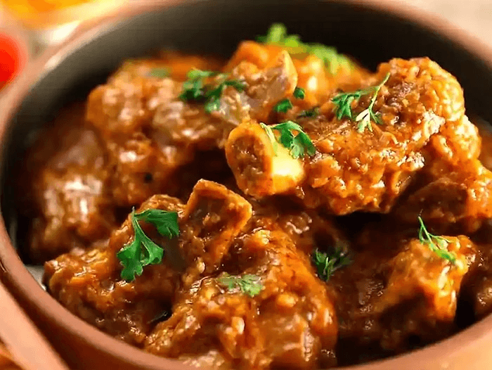 Authentic Chha Gosht, a traditional Chamba delicacy meaning 'lamb cooked on charcoal,' served at Jimmy's River Resort Chamba, featuring tender lamb pieces in a smoky, rich gravy garnished with fresh coriander.