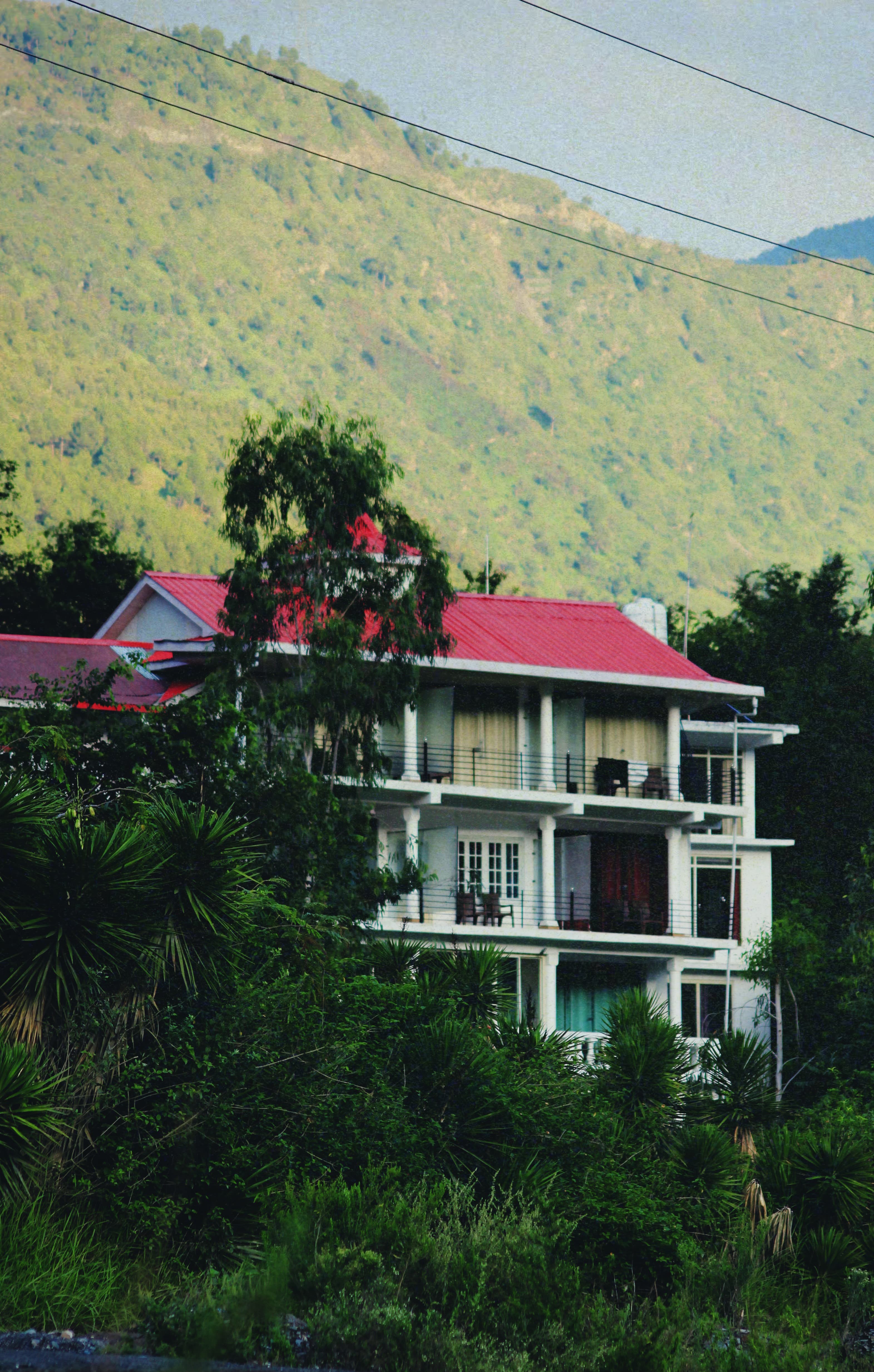 The main building of Jimmy's River Resort Chamba, a multi-story structure with distinctive architecture, surrounded by lush greenery and scenic hills.