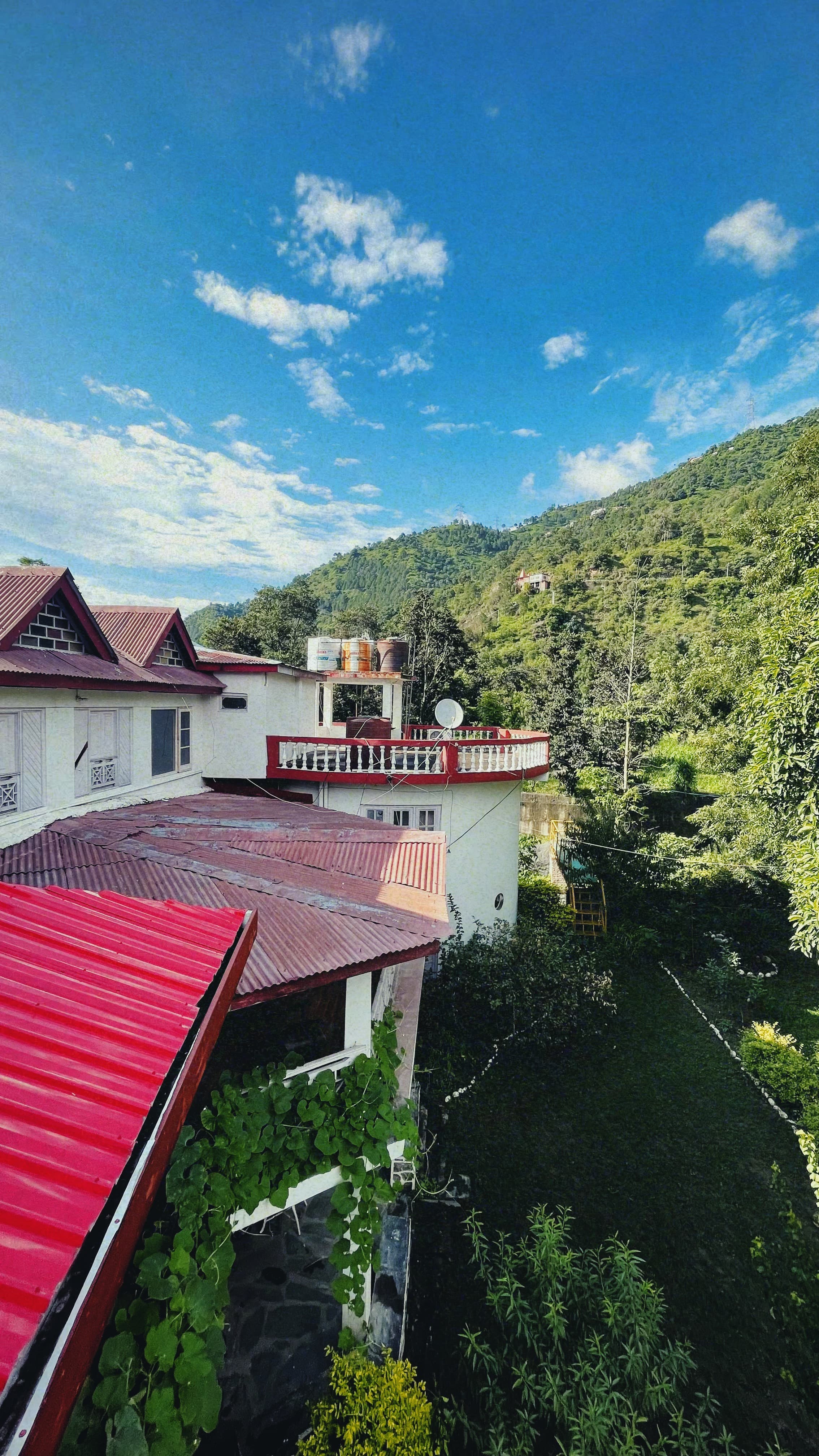 Jimmy's River Resort Chamba, nestled among verdant surroundings, with its vibrant rooftop standing out against the clear blue sky and rolling hills.