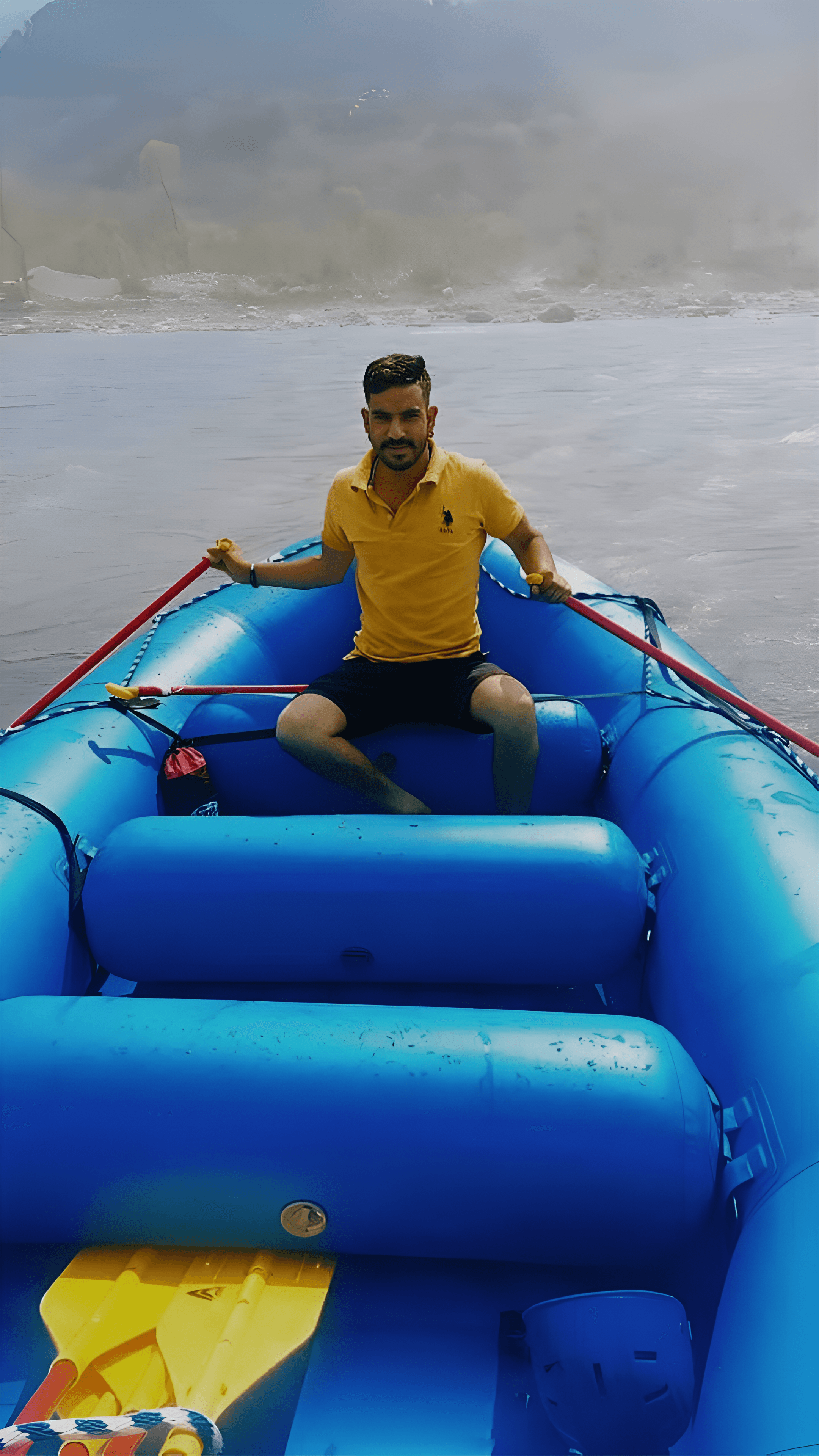 Rafting staff at Jimmy's River Resort Chamba, seated in a bright blue inflatable raft on the calm waters of the River Ravi with a misty natural backdrop.