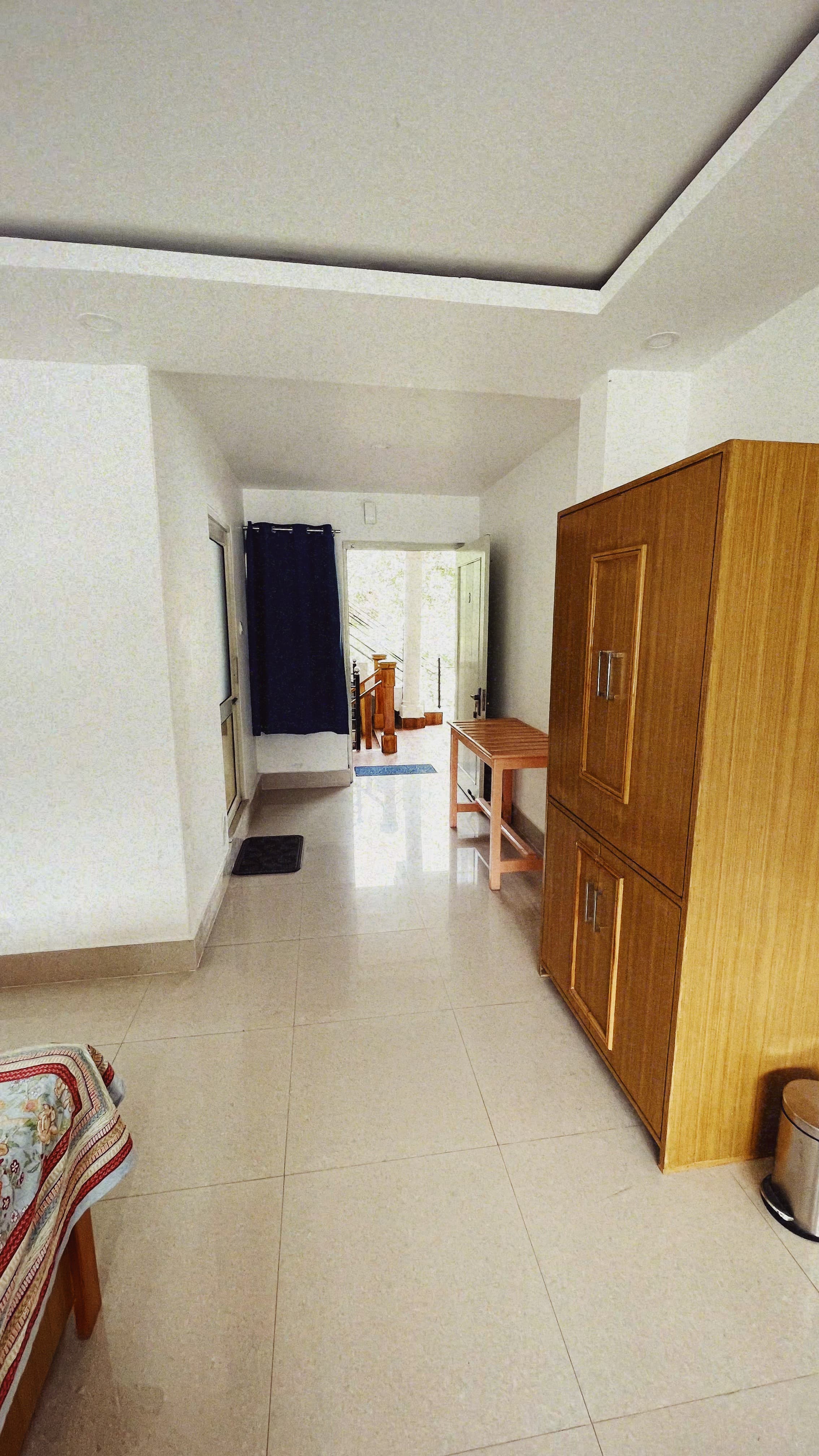 A wide view of a comfortable room at Jimmy's River Resort Chamba, showcasing sleek tiled floors, a double bed, and access to an outdoor area through the hallway.